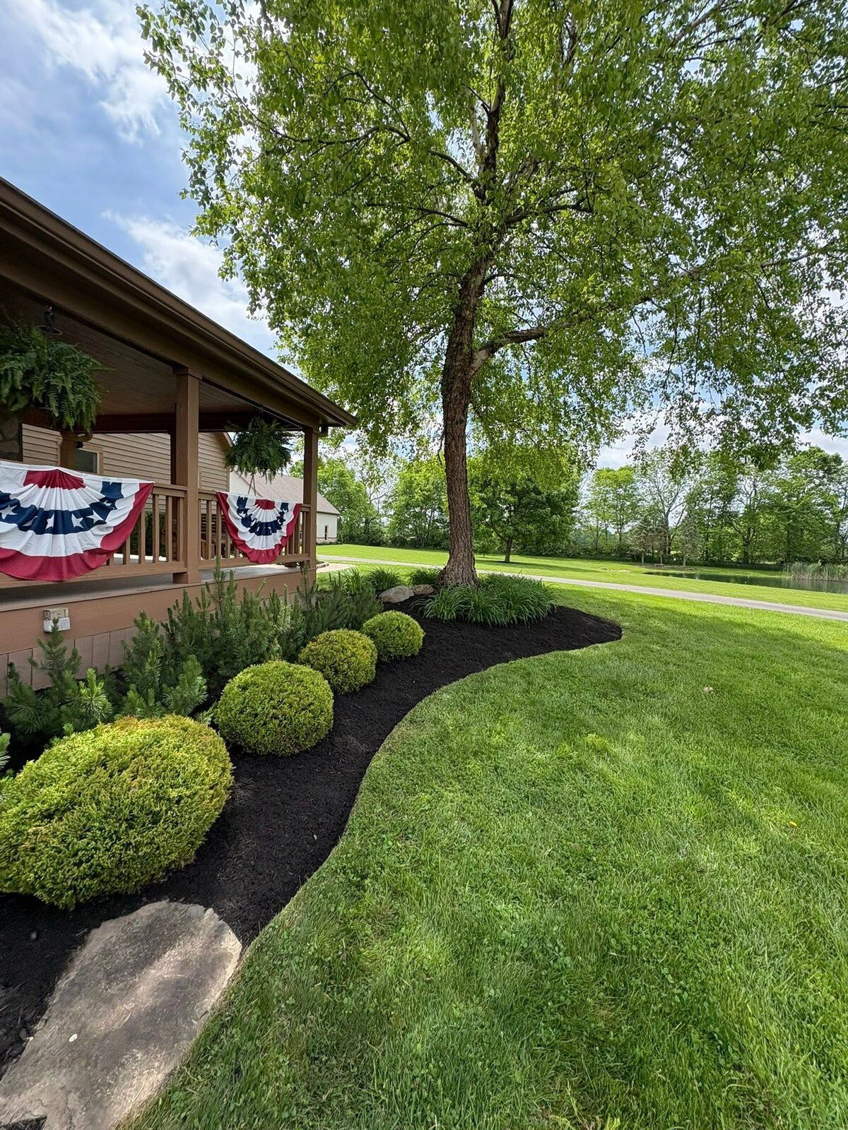 Curved mulch bed, ornamental tree and boxwoods by a front porch