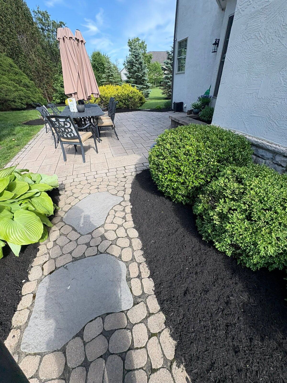 Paver patio and stone walkway framed by fresh curved mulch beds